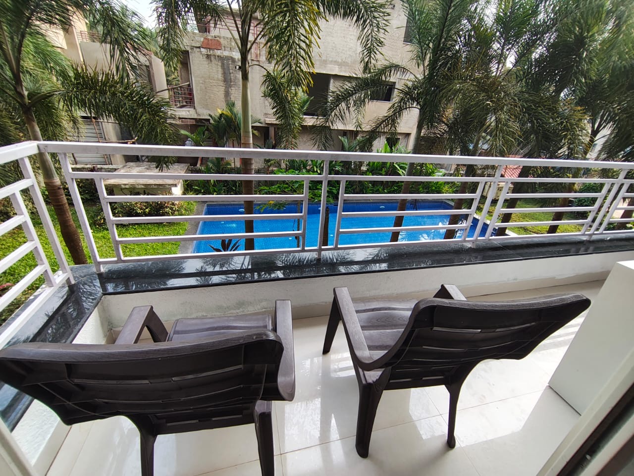 Private balcony with chairs overlooking the pool and palm-lined courtyard